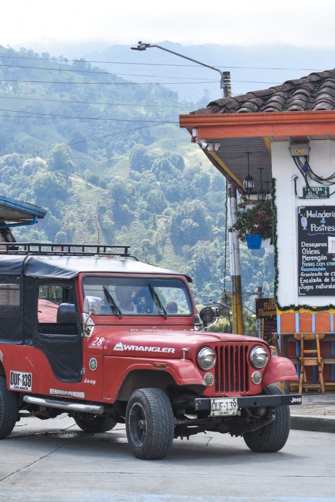 A classic red Jeep Wrangler is parked on a vibrant street in a Colombian town.